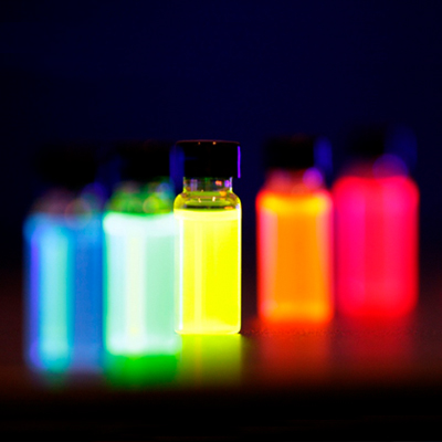 Photo of five small bottles of liquid, glowing red, orange, yellow, green, and blue against a black background.